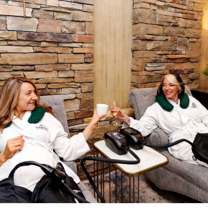 - The Renaissance Day Spa & Alternative Wellness, Fayetteville NC Two women in white robes relax in lounge chairs, clinking a coffee cup and a wine glass, with massage devices on their legs in a spa setting. - The Renaissance Day Spa & Alternative Wellness, Fayetteville NC