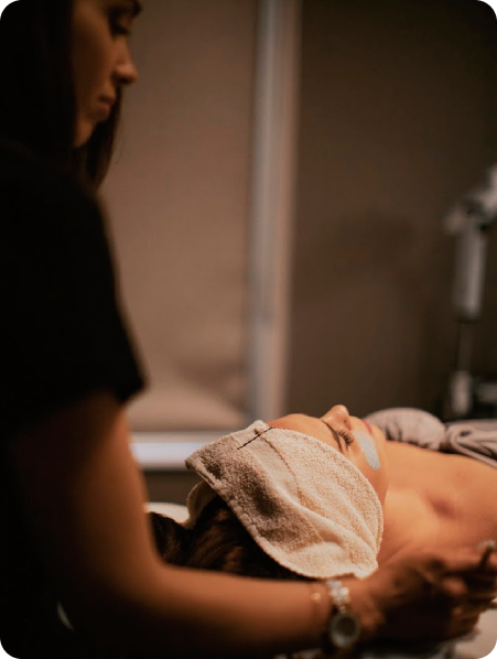 - The Renaissance Day Spa & Alternative Wellness, Fayetteville NC A person lies on a treatment table with a towel covering their face while another stands nearby, suggesting a holistic alternative therapy or deep tissue massage therapy session in progress. - The Renaissance Day Spa & Alternative Wellness, Fayetteville NC