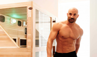 - The Renaissance Day Spa & Alternative Wellness, Fayetteville NC A shirtless, muscular man stands beside a wooden sauna in a brightly lit room. - The Renaissance Day Spa & Alternative Wellness, Fayetteville NC