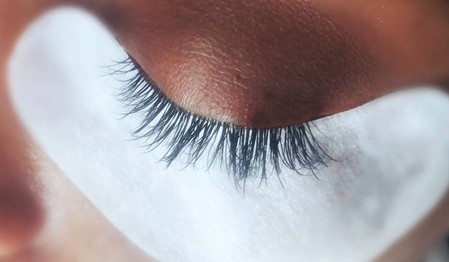 - The Renaissance Day Spa & Alternative Wellness, Fayetteville NC Close-up of a closed eye with long eyelashes and a white eye pad placed underneath the lower lashes, typically used during eyelash extension application. - The Renaissance Day Spa & Alternative Wellness, Fayetteville NC