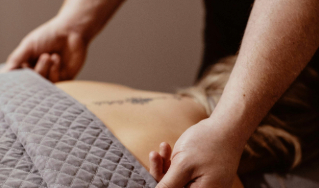 - The Renaissance Day Spa & Alternative Wellness, Fayetteville NC Person receiving a back massage, with a visible tattoo on their upper back and a gray quilted blanket covering their lower body. - The Renaissance Day Spa & Alternative Wellness, Fayetteville NC