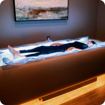 - The Renaissance Day Spa & Alternative Wellness, Fayetteville NC A person in dark clothing lies on a spa bed under soft lighting, with a painting above them, enjoying deep tissue massage therapy for ultimate relaxation. - The Renaissance Day Spa & Alternative Wellness, Fayetteville NC